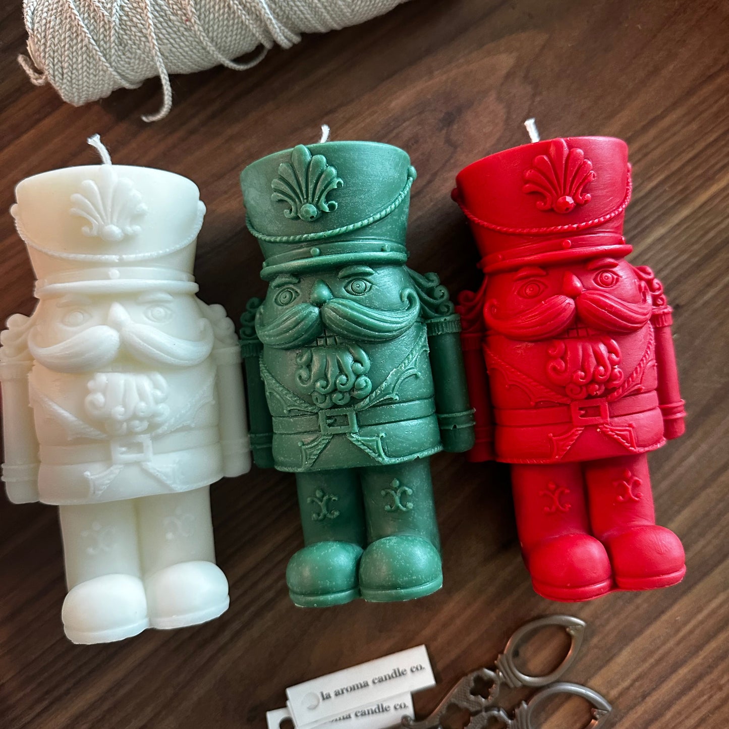 Three colorful candles shaped like a warrior figure on a wooden surface with twine and scissors.