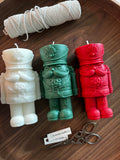 Three colorful candles shaped like a warrior figure on a wooden surface with twine and scissors.