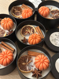 Decorative candles with pumpkin and cinnamon elements in black containers.